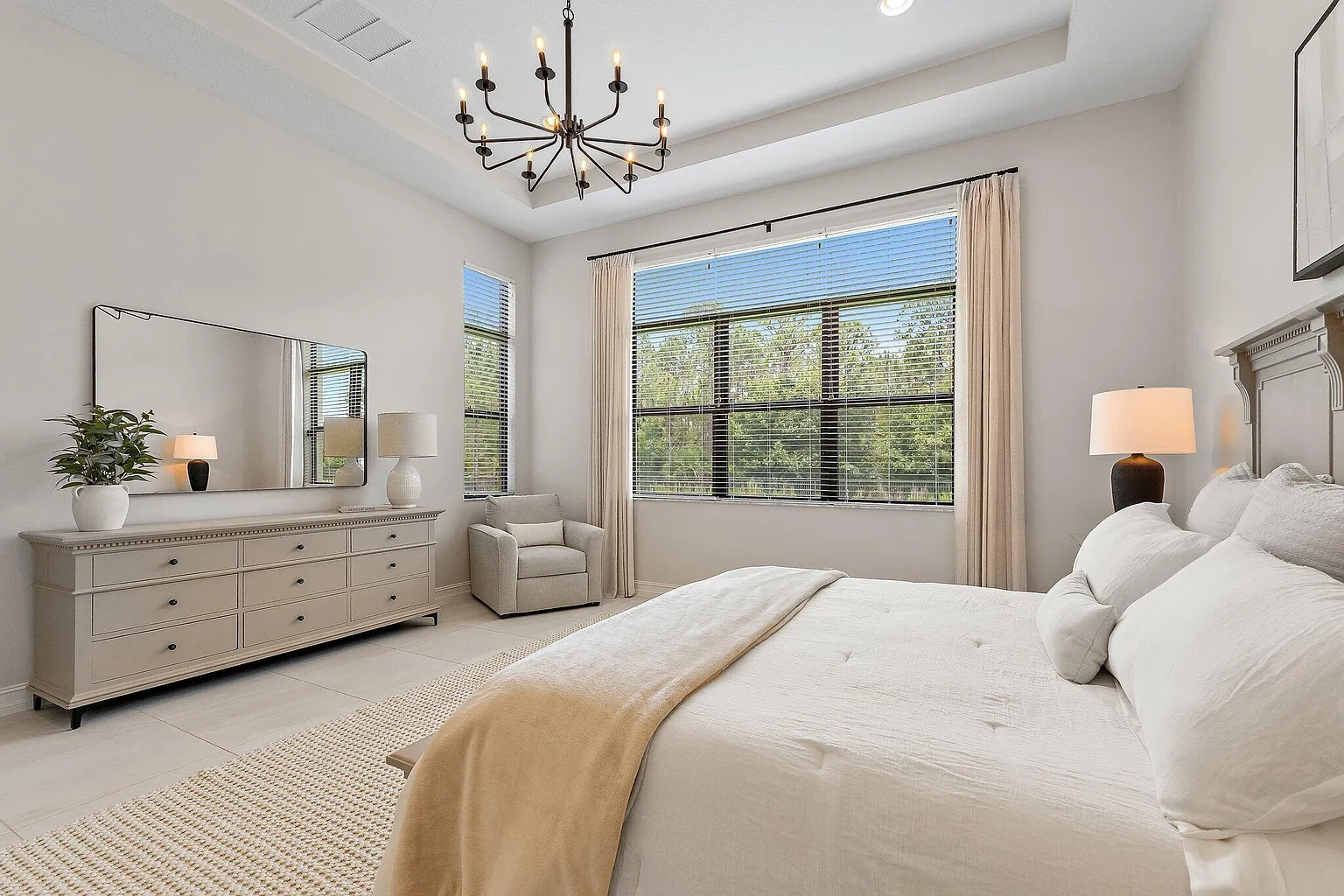 Bedroom with tray ceiling, dresser with mirror, and bright windows