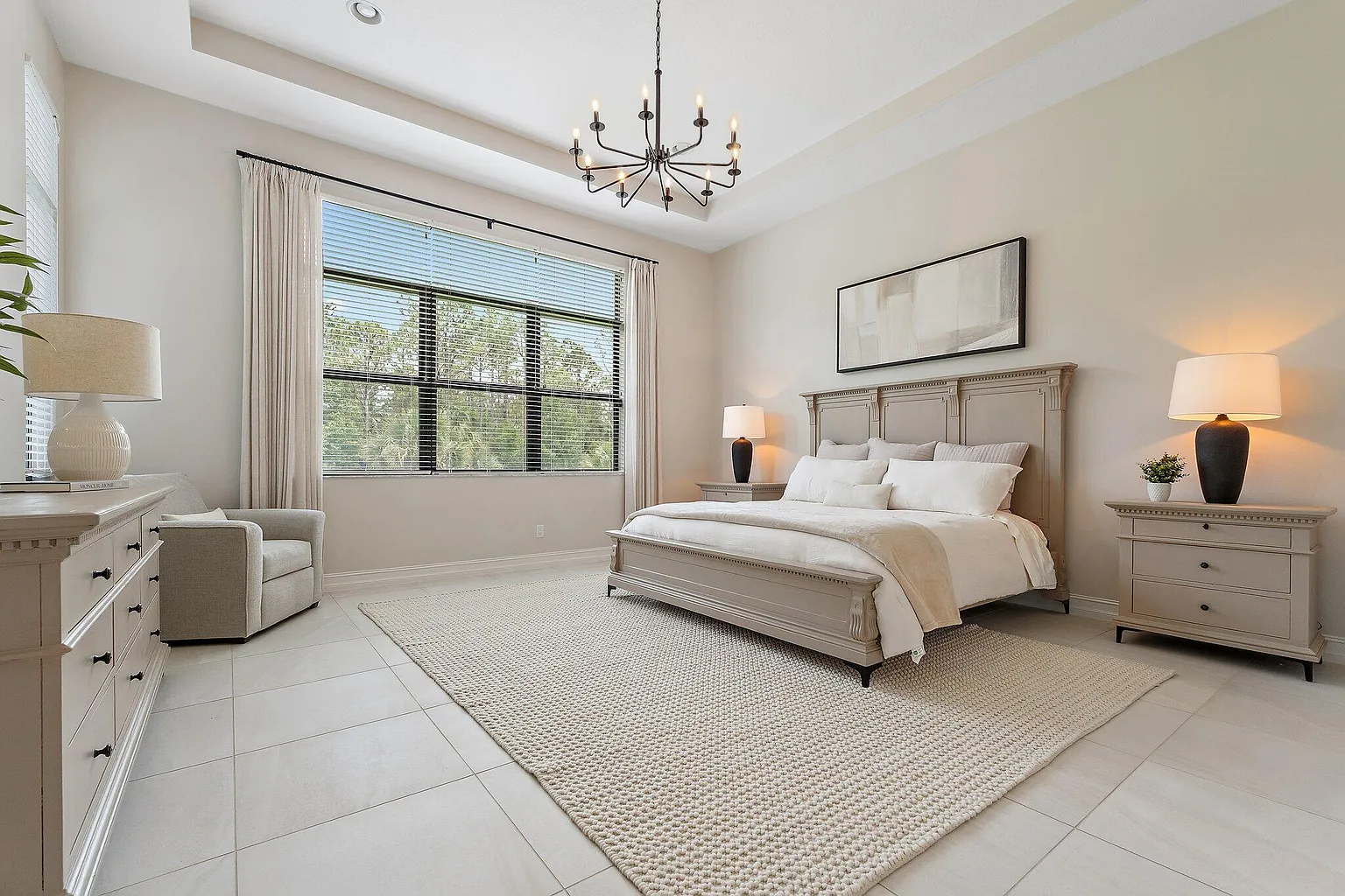 Primary bedroom with tray ceiling, chandelier, and large window